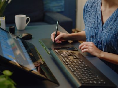 Close up of photo editing equipment at photography studio on desk. Woman working as editor using retouching software, keyboard and graphic tablet with stylus for retouch media project
